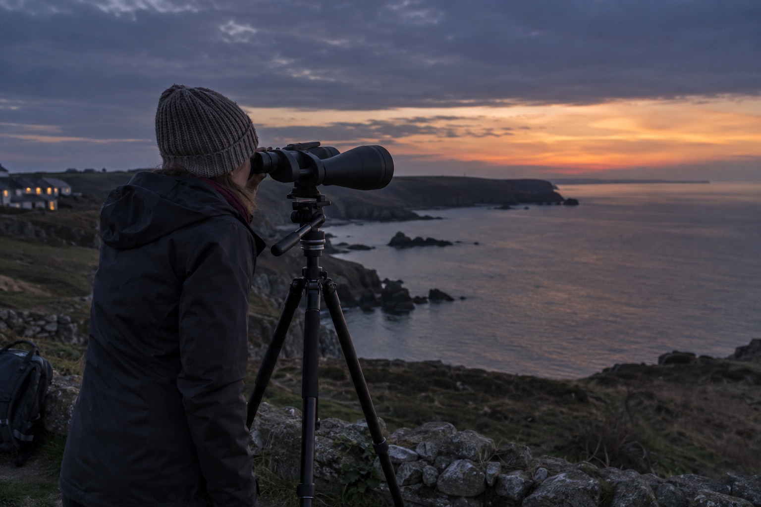 Large unbranded binoculars on a sturdy tripod at a coastal viewpoint at dusk